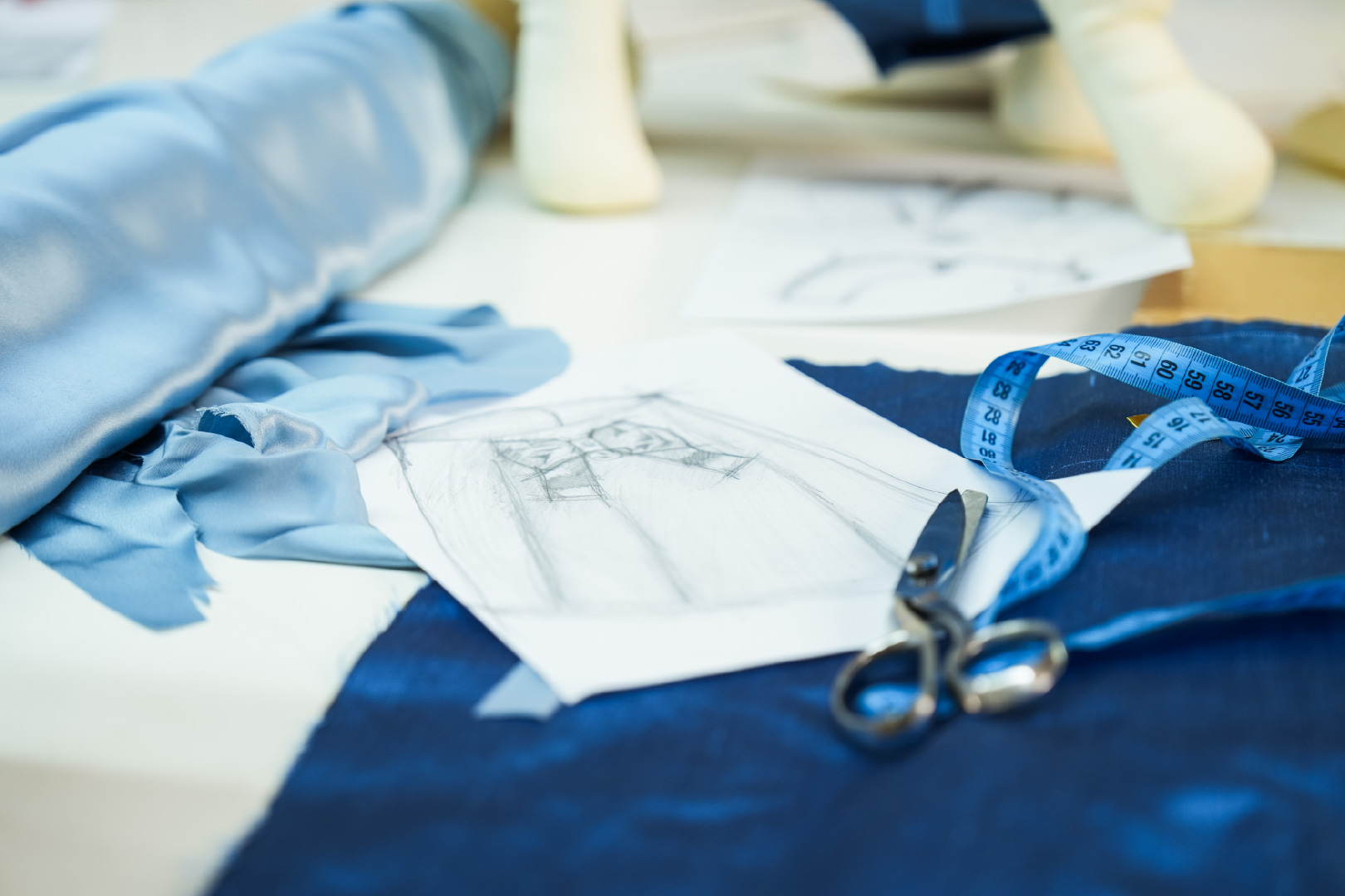 Blue Italian silk, a pencil pattern sketch, tailor's shears and a tape measure on the atelier cutting table